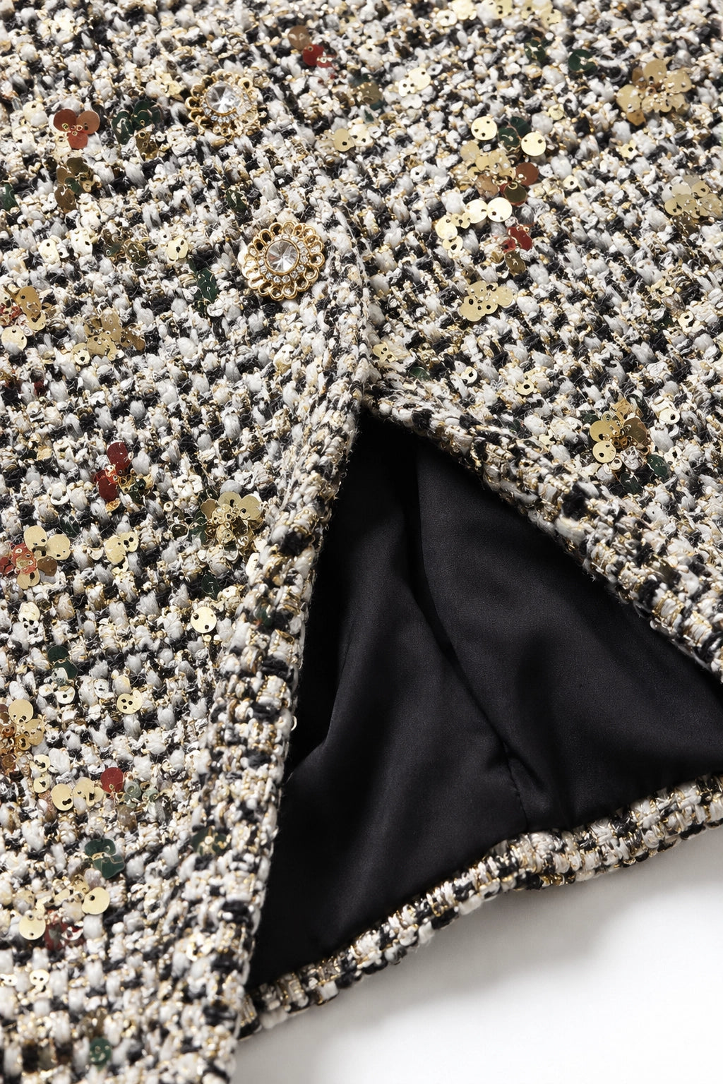 Close-up of a textured tweed fabric with dense sequins in black, white, gold, and red, showing a black satin lining folded over.