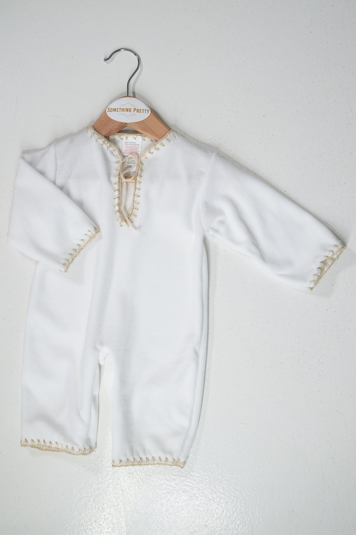 White baby outfit with gold trim on a hanger against a white background