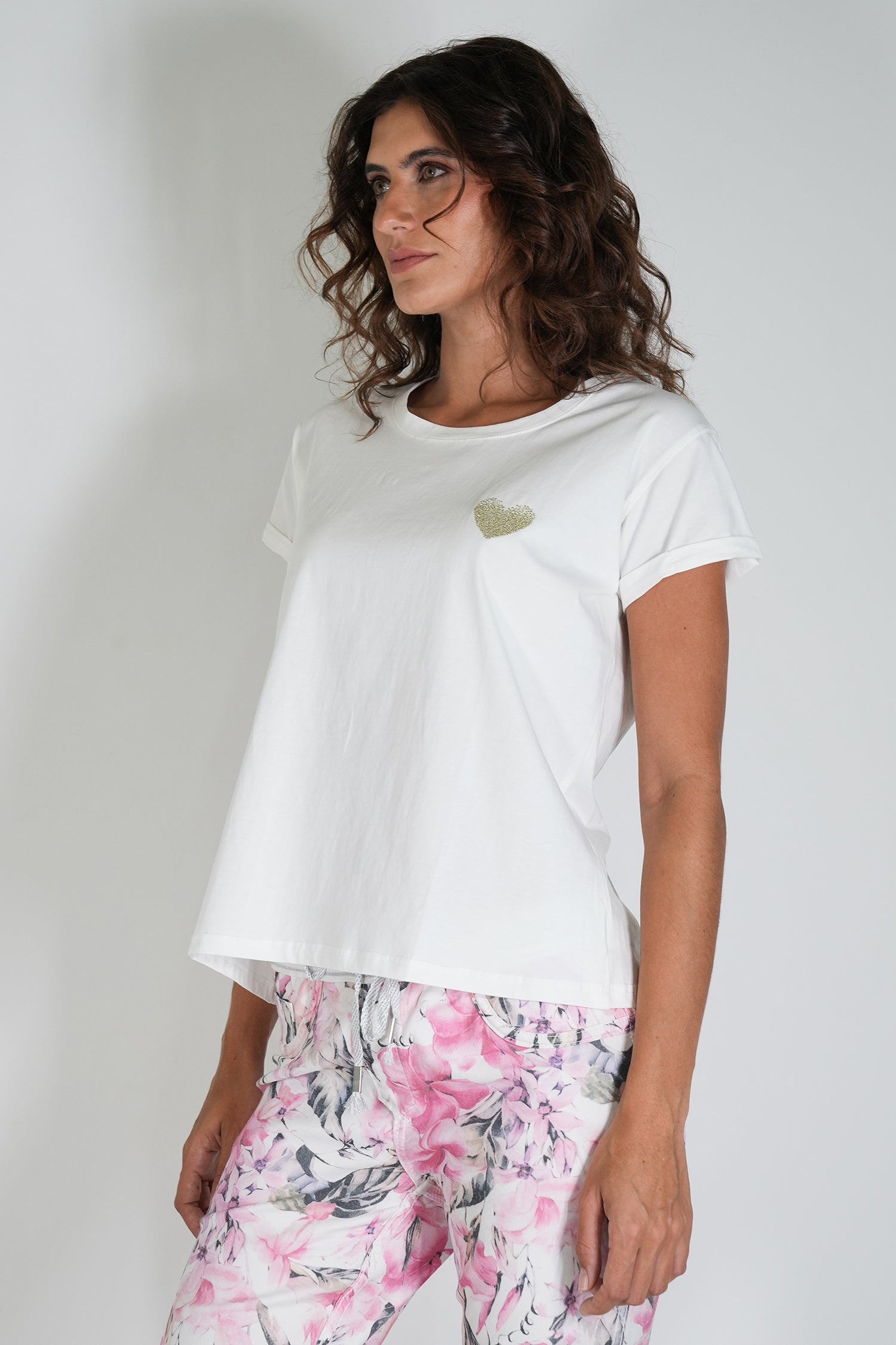 Woman wearing a white t-shirt with a small design and floral pants on a plain background