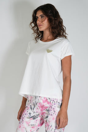 Woman wearing a white t-shirt with a small design and floral pants on a plain background