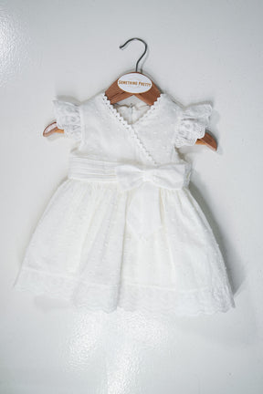 White baby dress with lace details on a wooden hanger against a white background