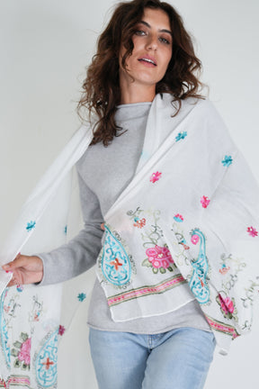 Woman wearing a white embroidered shawl with colorful designs on a plain background