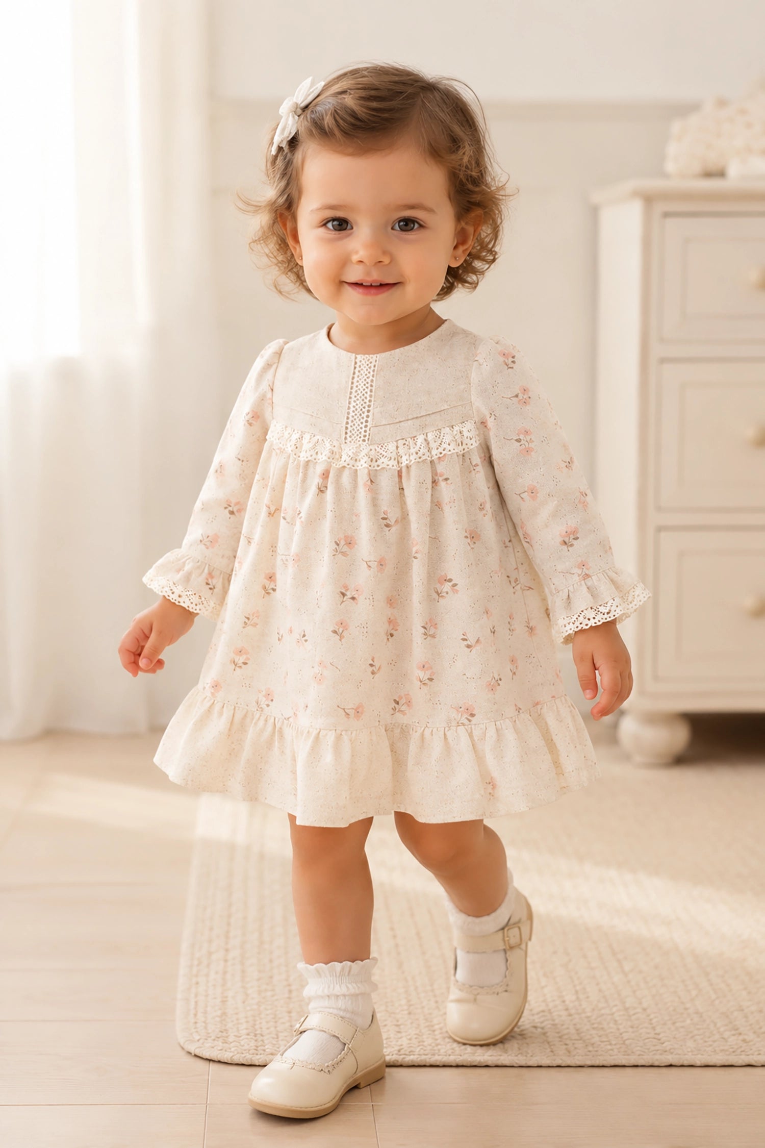 Young girl in a beige dress with floral patterns standing in a softly lit room.
