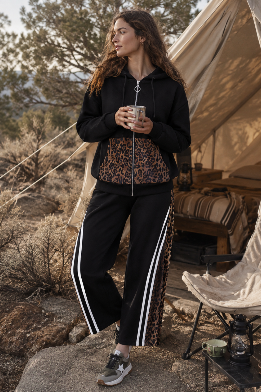 Woman in black tracksuit with white stripes holding a mug near a tent in a natural setting