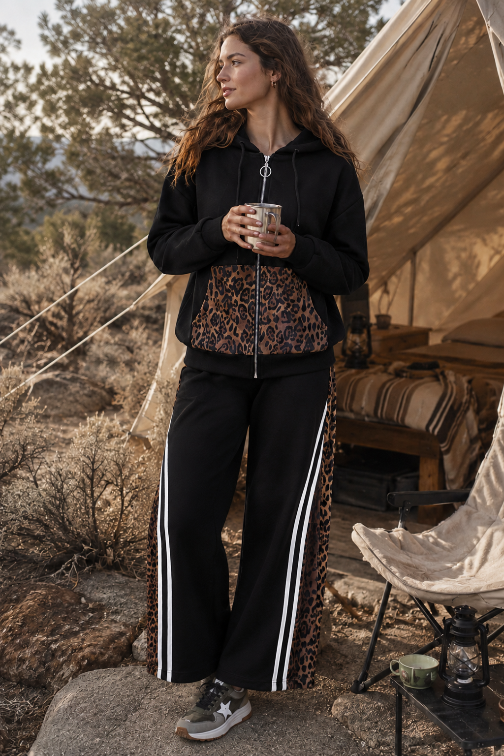 Woman standing outdoors near a tent holding a mug, wearing a black tracksuit with leopard print top.