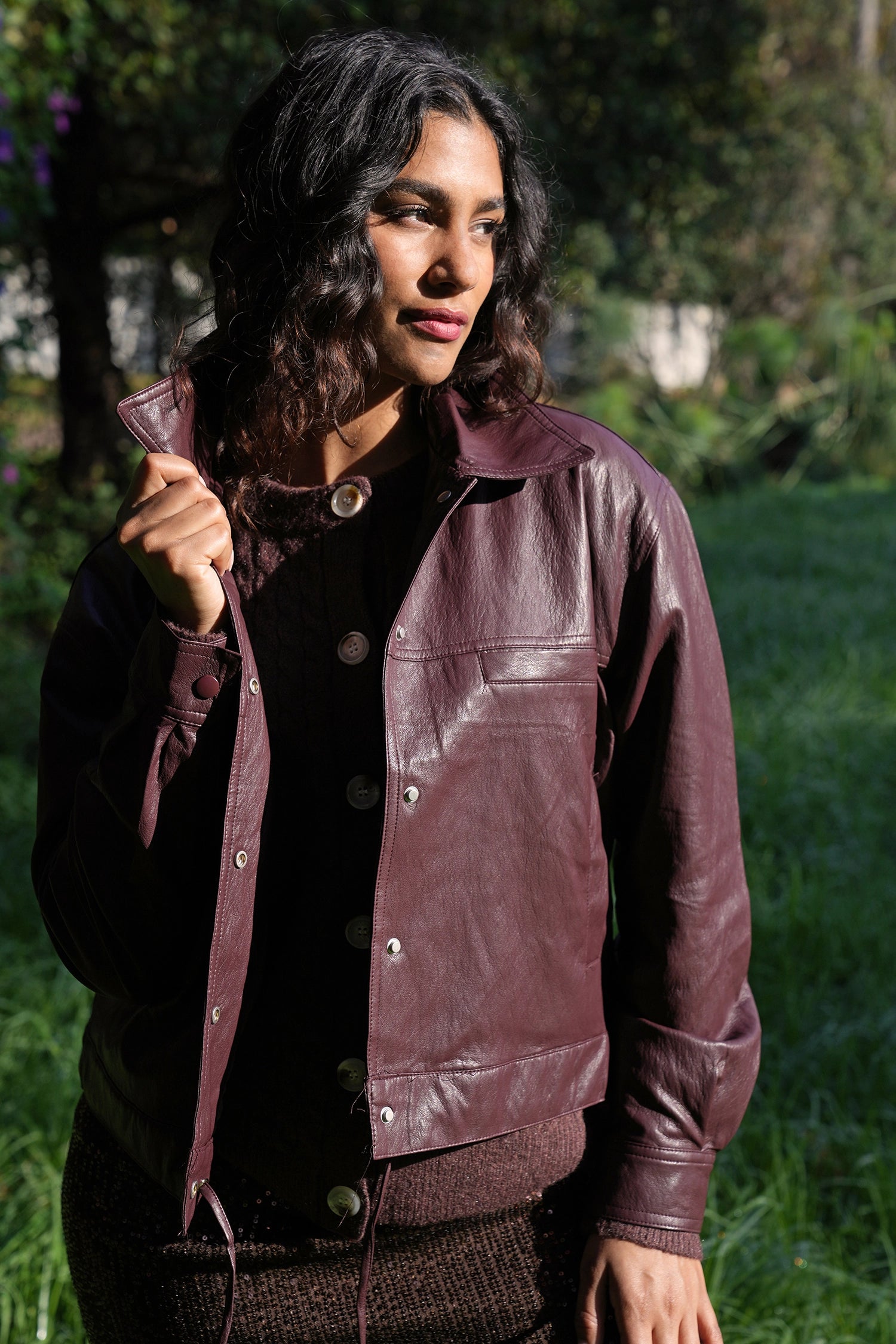 Woman wearing a dark leather jacket outdoors with greenery in the background