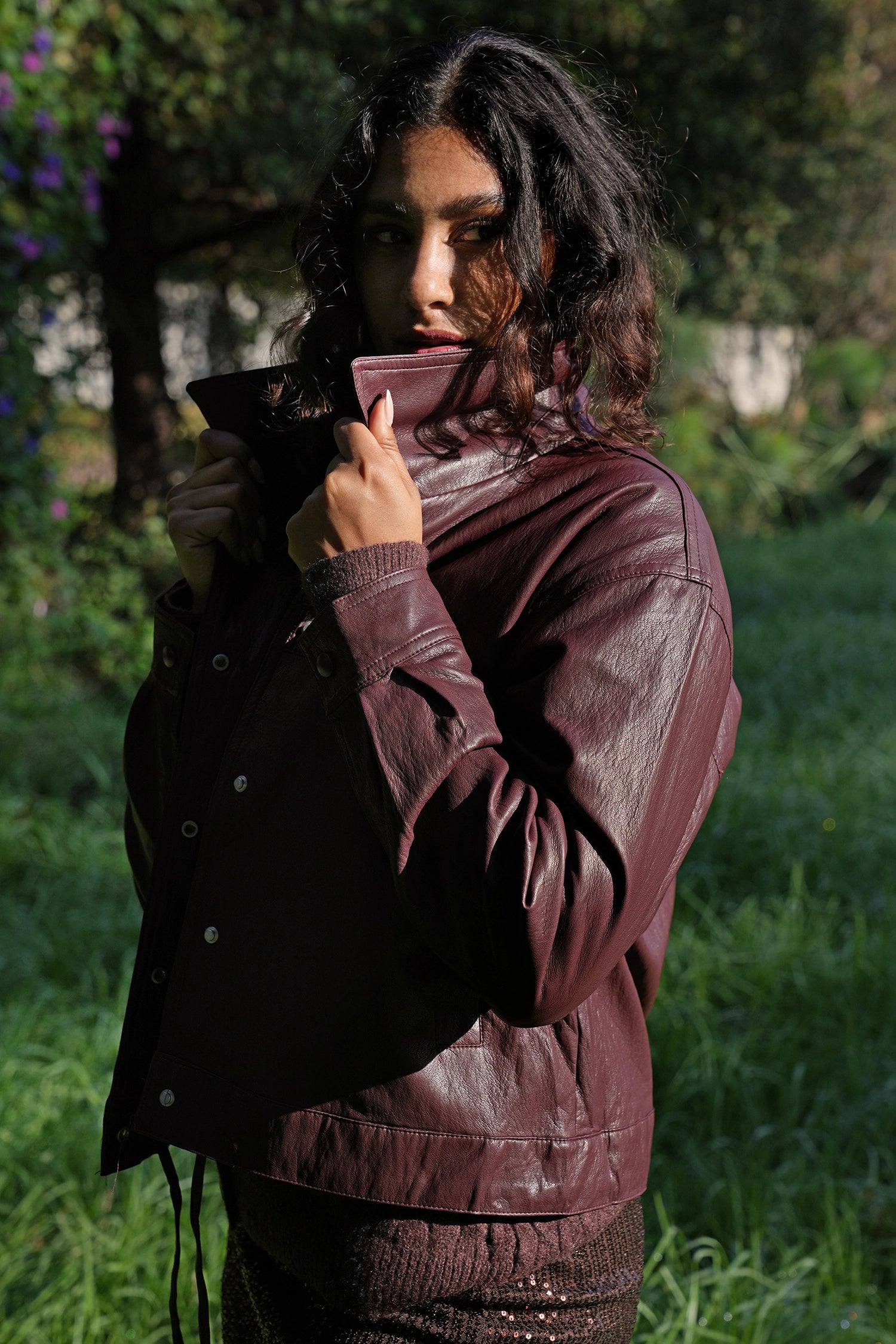 Person wearing a burgundy leather jacket in a garden setting
