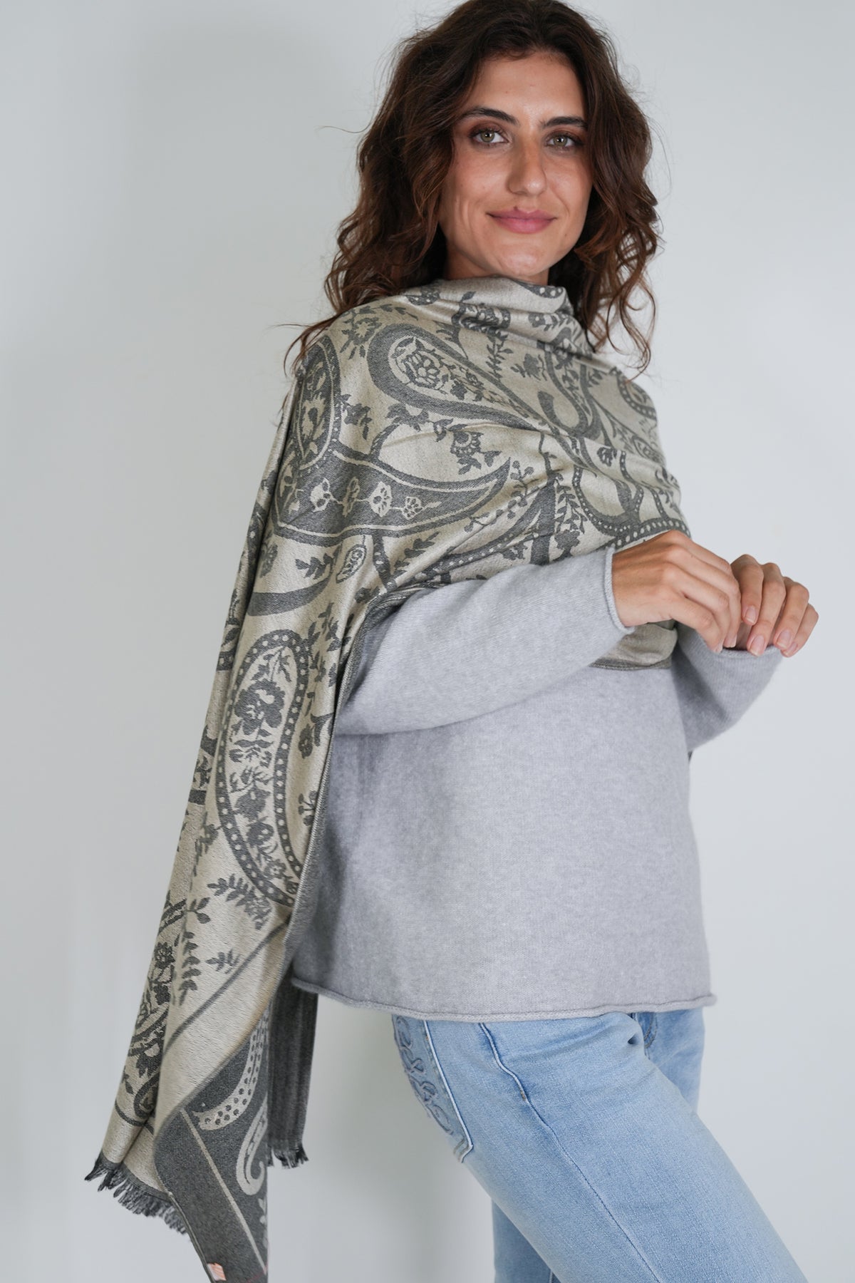 Woman wearing a patterned scarf, gray sweater, and blue jeans against a white background