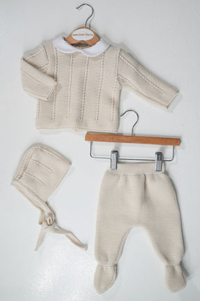 Baby sweater, hat, and pants set on hangers against a white background