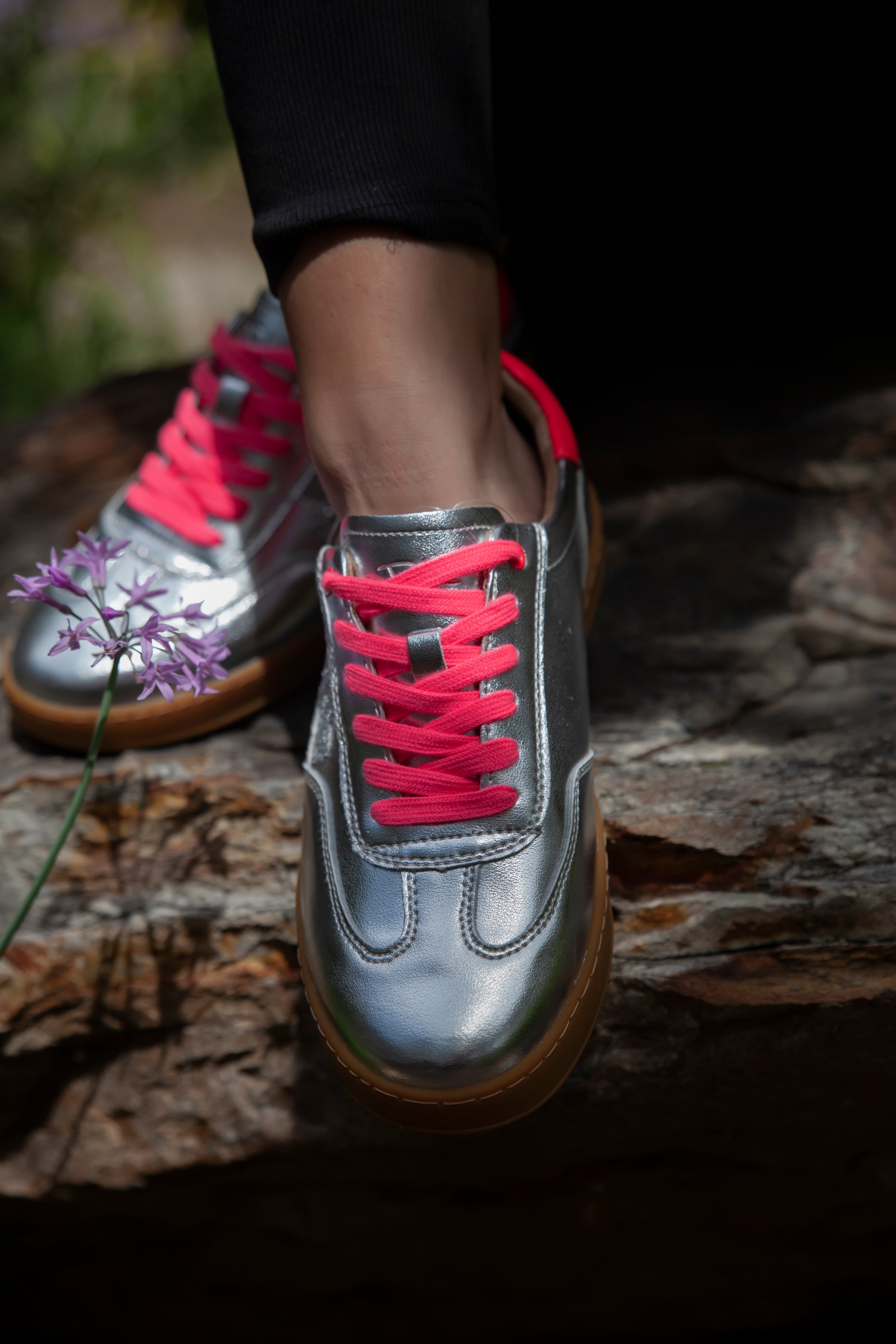 Silver sneakers with pink laces worn on a stone surface