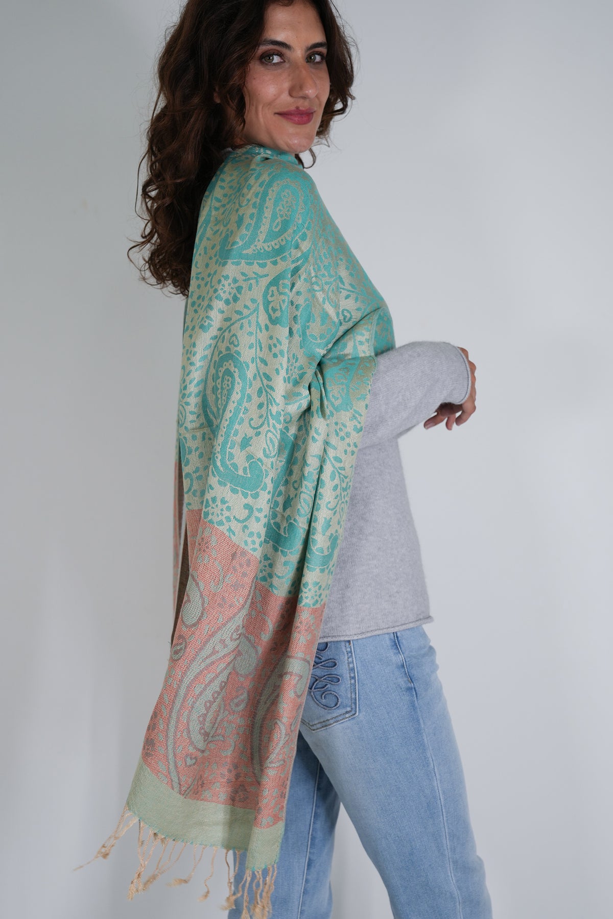 Woman wearing a teal and pink patterned scarf on a plain background