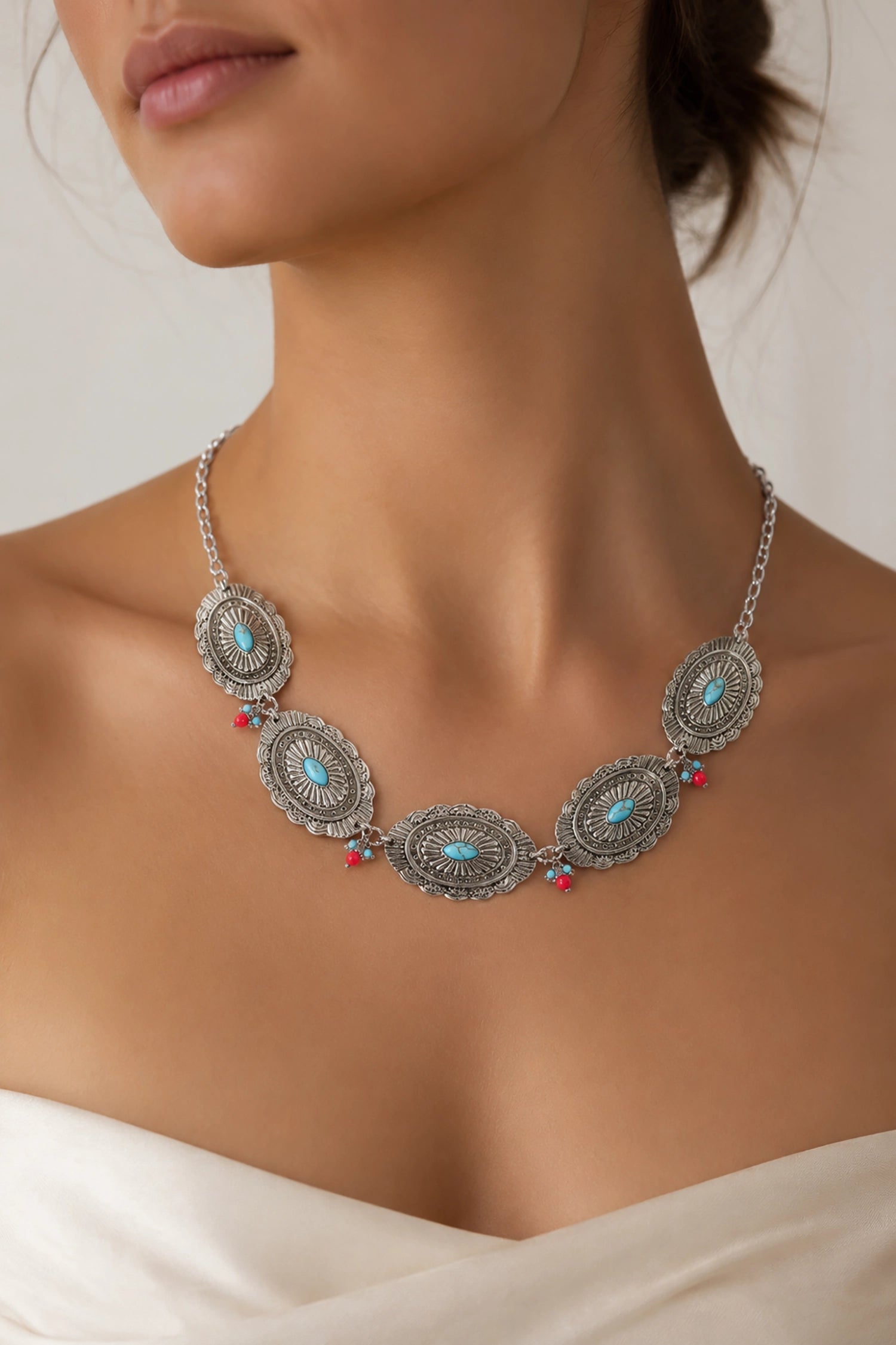 Silver necklace with turquoise and red stones worn by a model against a neutral background